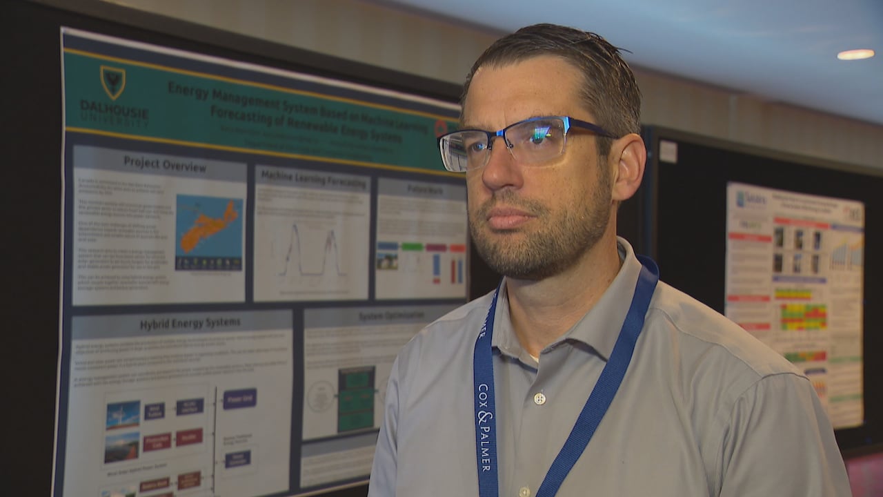 A white man with short, dark hair is seen wearing glasses and a grey, short-sleeved polo.