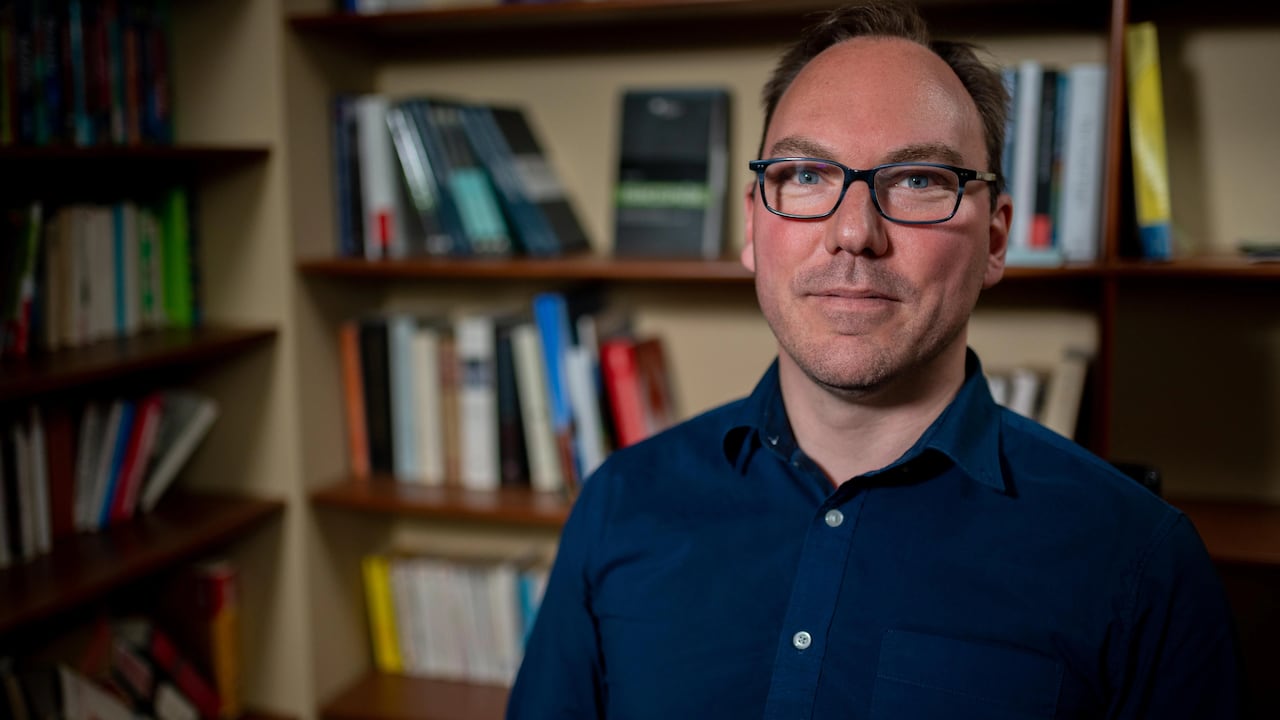 A man with glasses standing in front of a bookshelf.