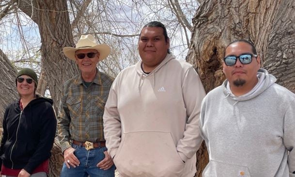 Four people stand in front of a tree. 