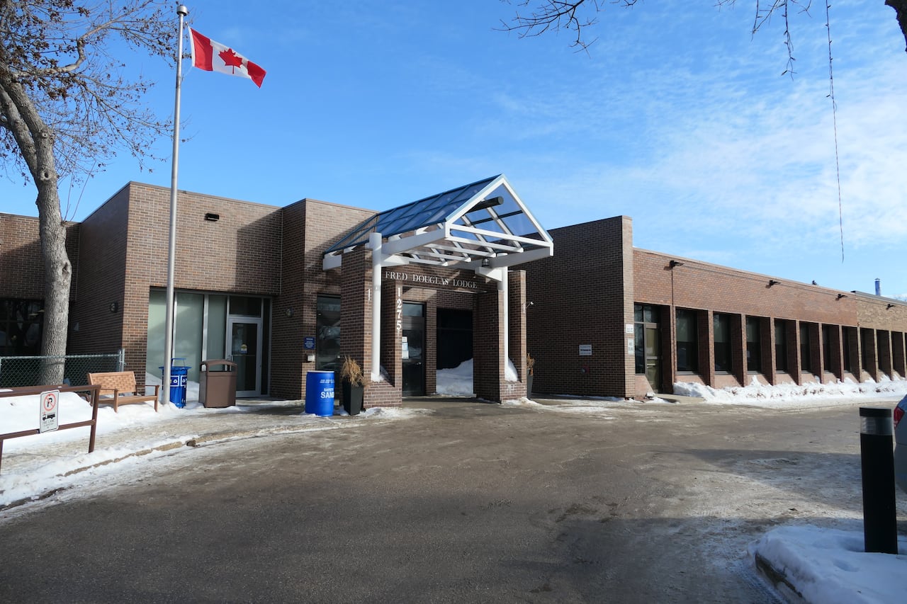 A driveway with snow beside it leads to a brown one-storey commercial building with a Canadian flag beside it. 