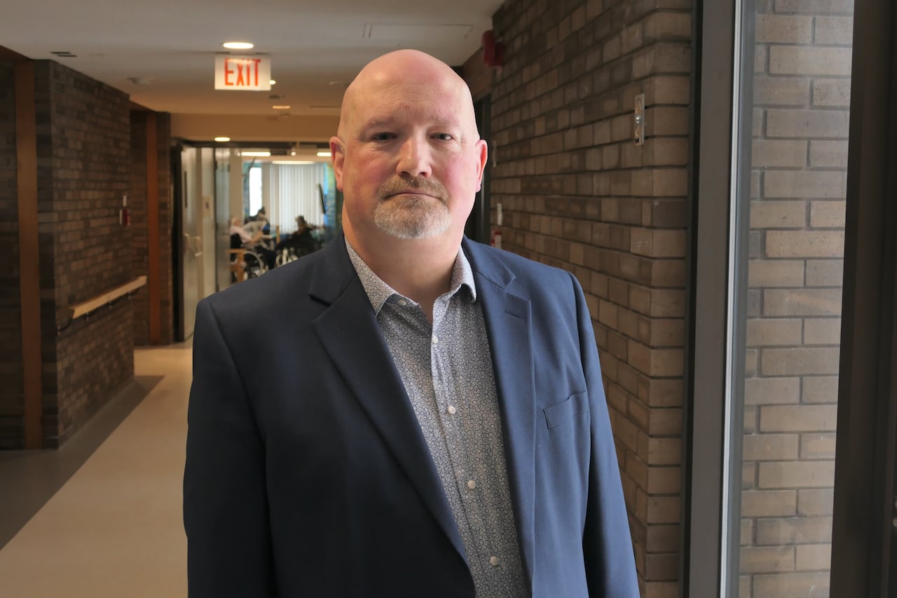 A man in a suit jacked stands in the hallway of a building with brick walls.