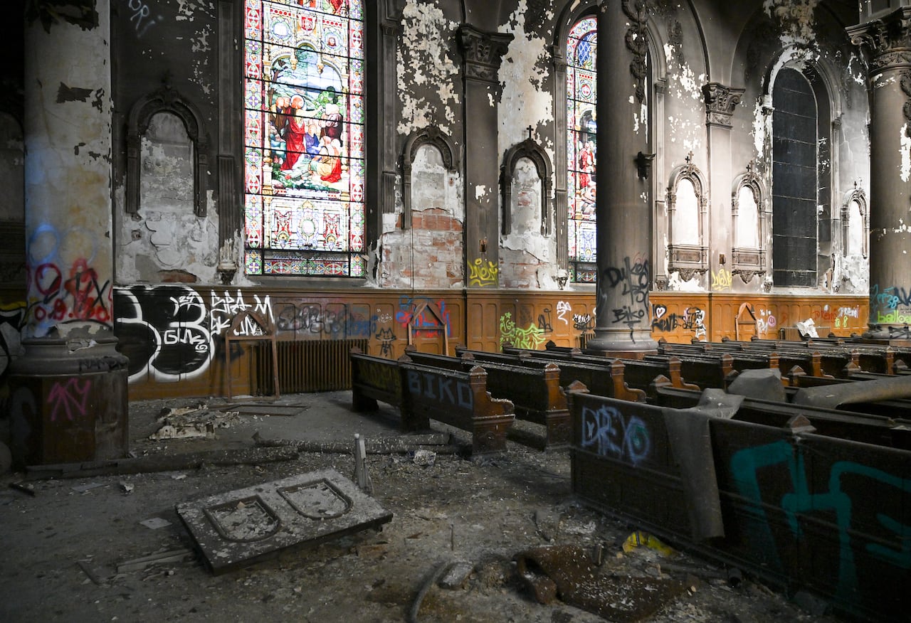 Broken pews, graffiti and debris are seen inside a church. 