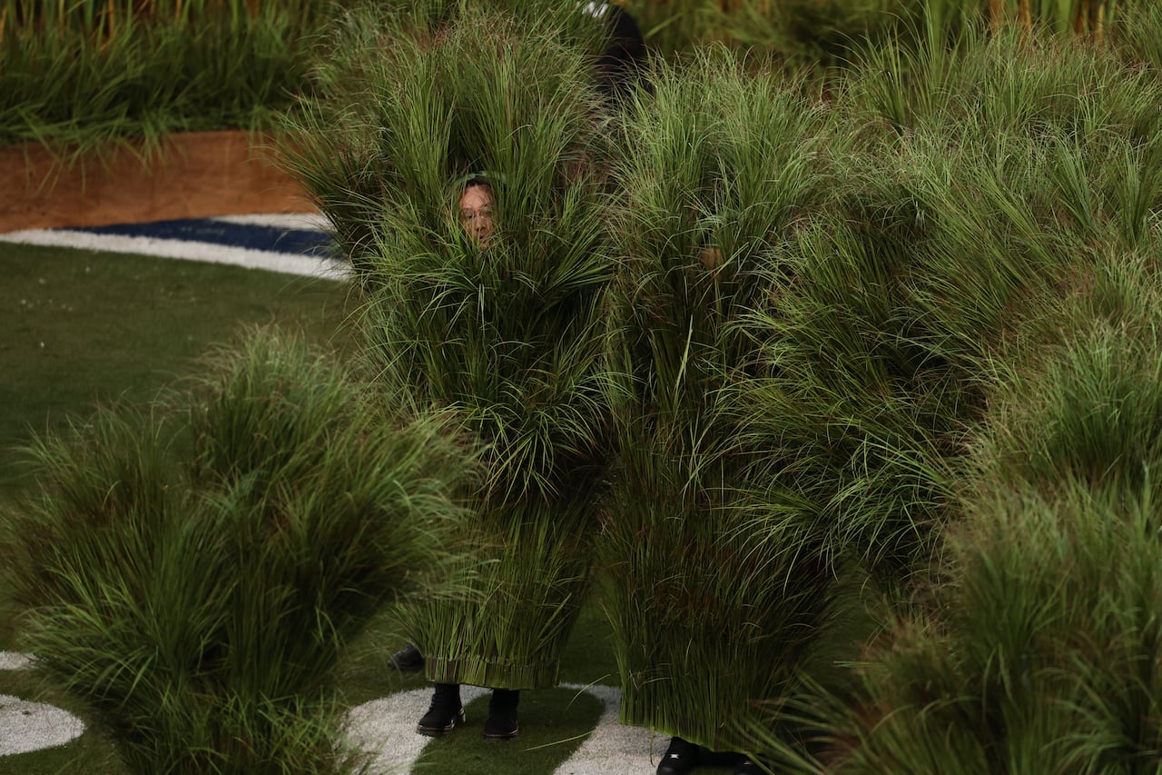 Several tall bushels of grass, from which can be seen human faces peeking out at the top, and shoes at the bottom.