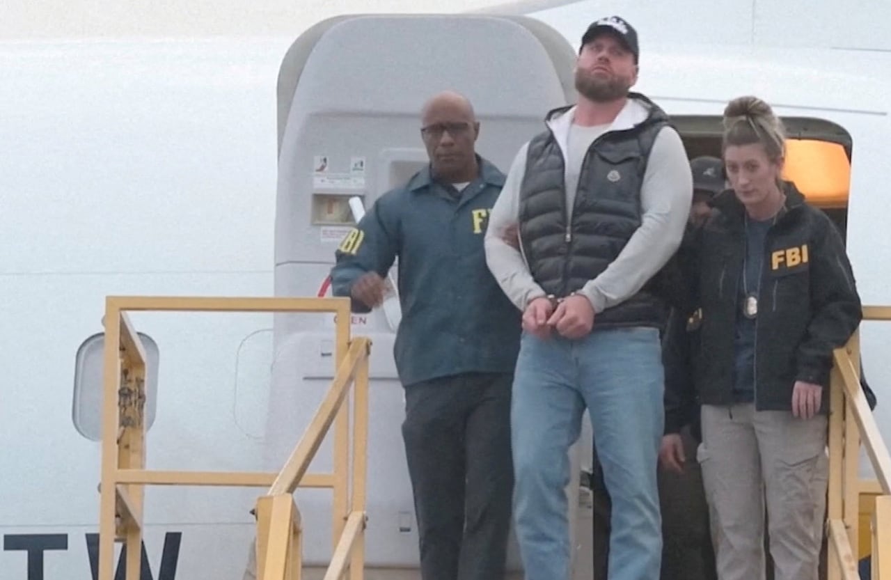 man in handcuffs being led off an airplane by two agents