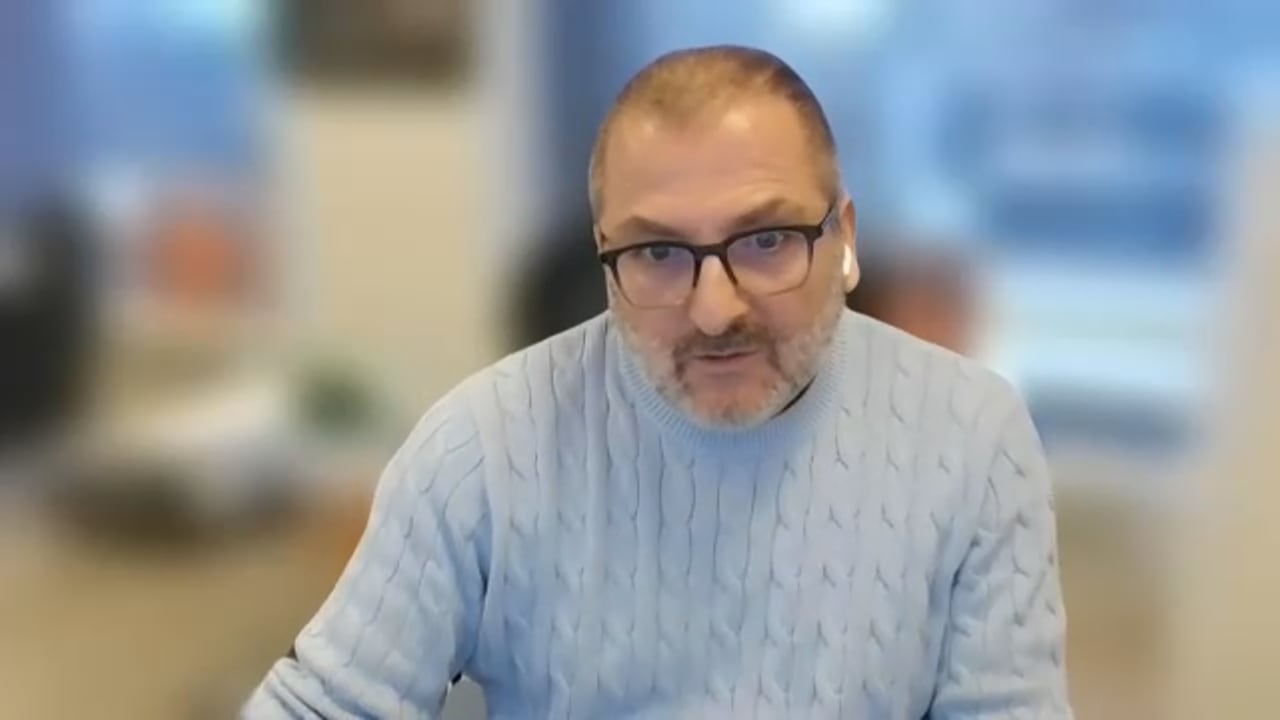A man in a blue sweater and glasses during a Zoom interview.