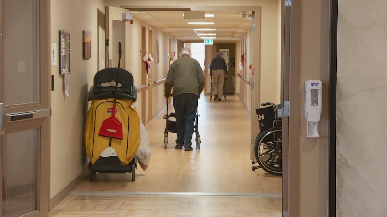 Man using walker to walk down the hall of a health-care facility.