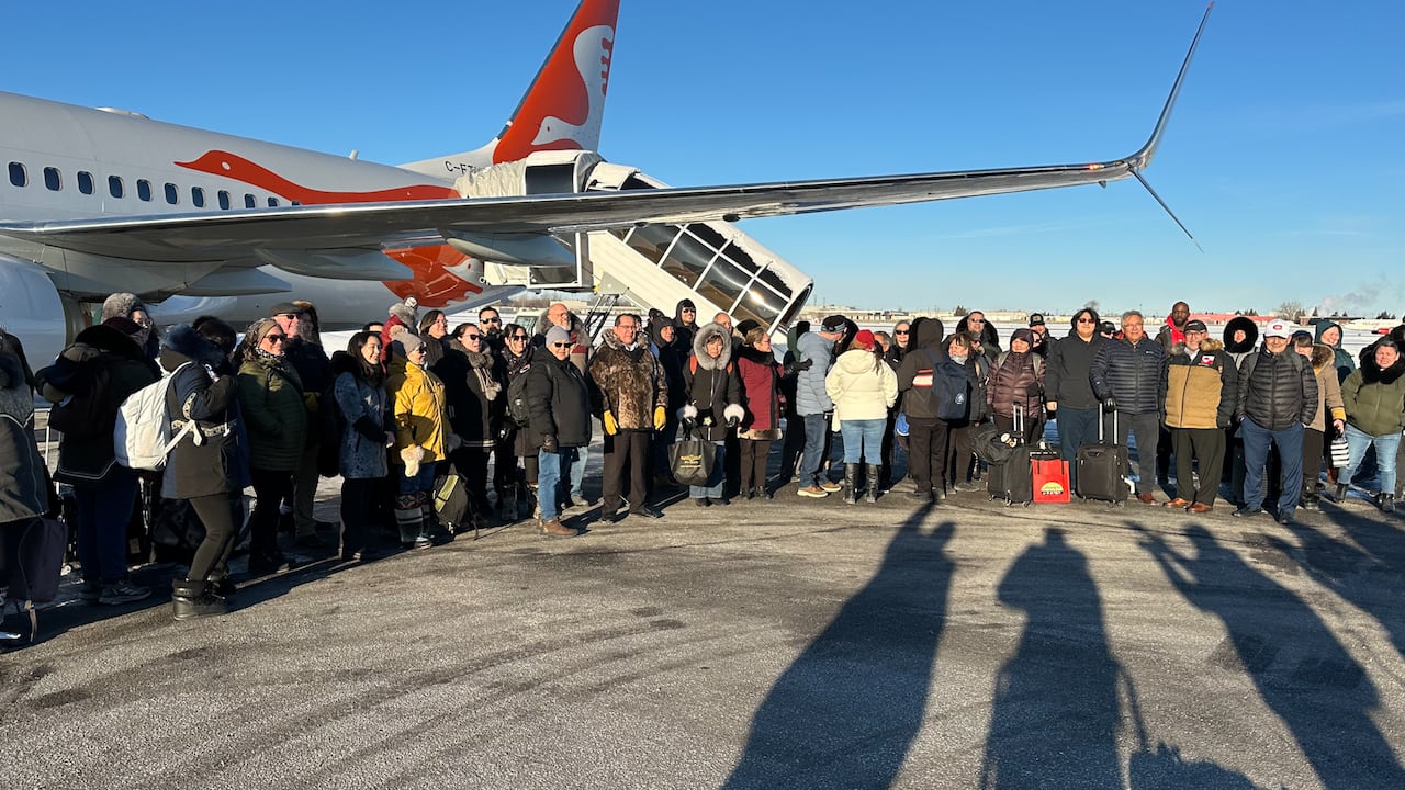 A long line of people pose for a photo in front of an airplane