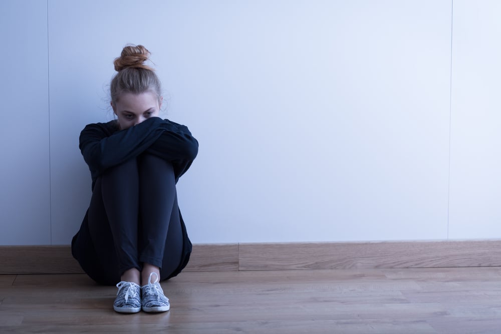 A young woman sits on the floor with her head resting on her knees.