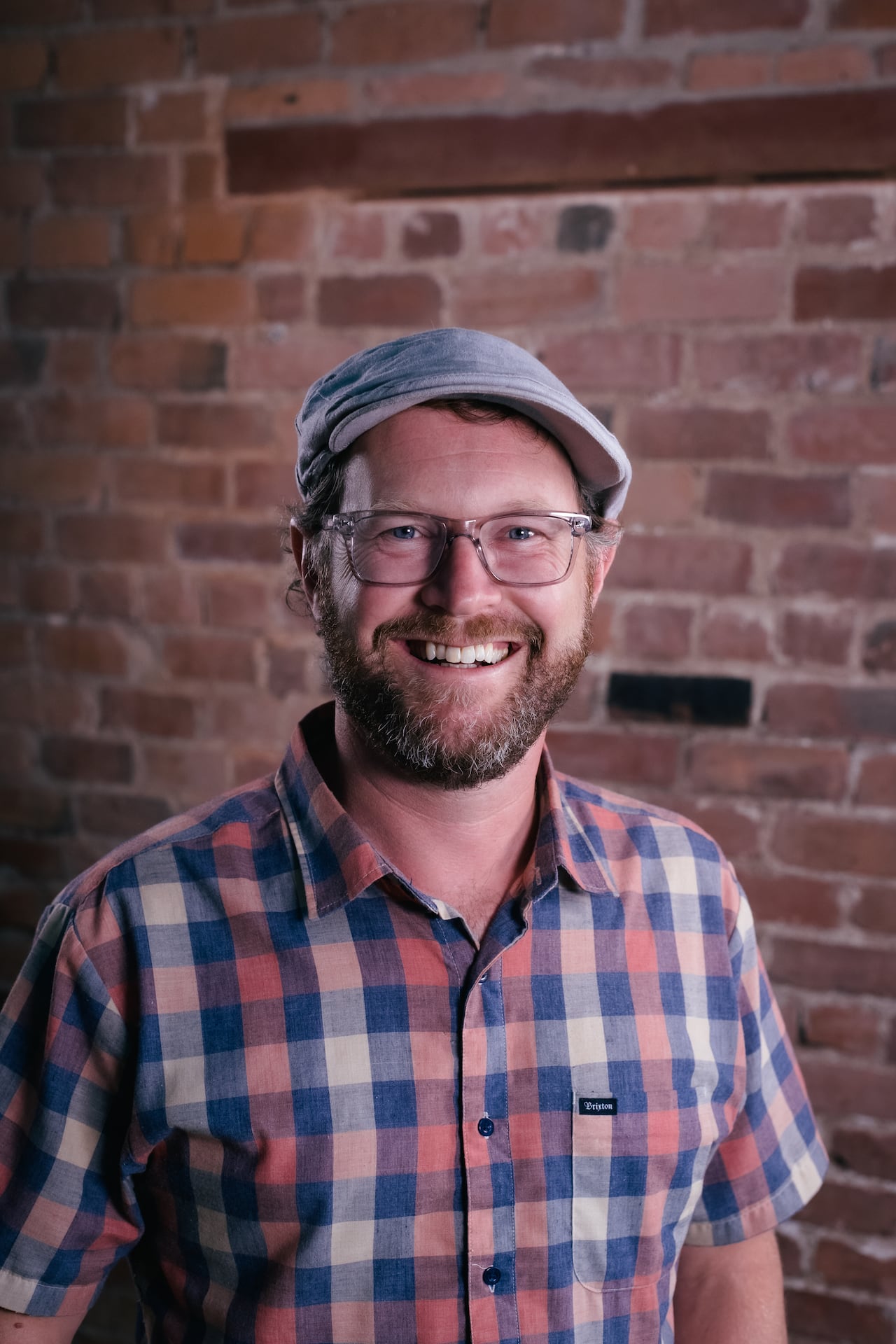 Man smiling at camera with a brick wall behind him. 