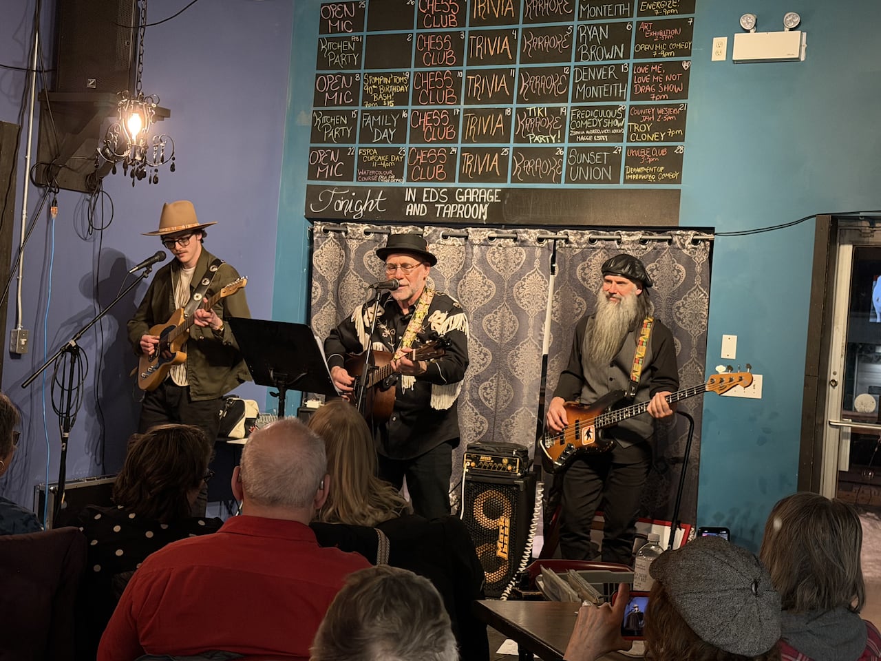 Three men with guitars/bass on stage doing a musical performance on stage in front of audience. 