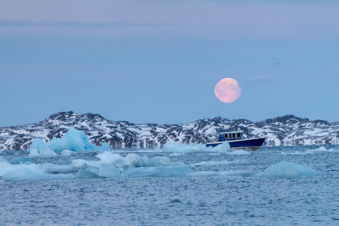 A full moon in the sky as the sun rises near Nuuk harbour.