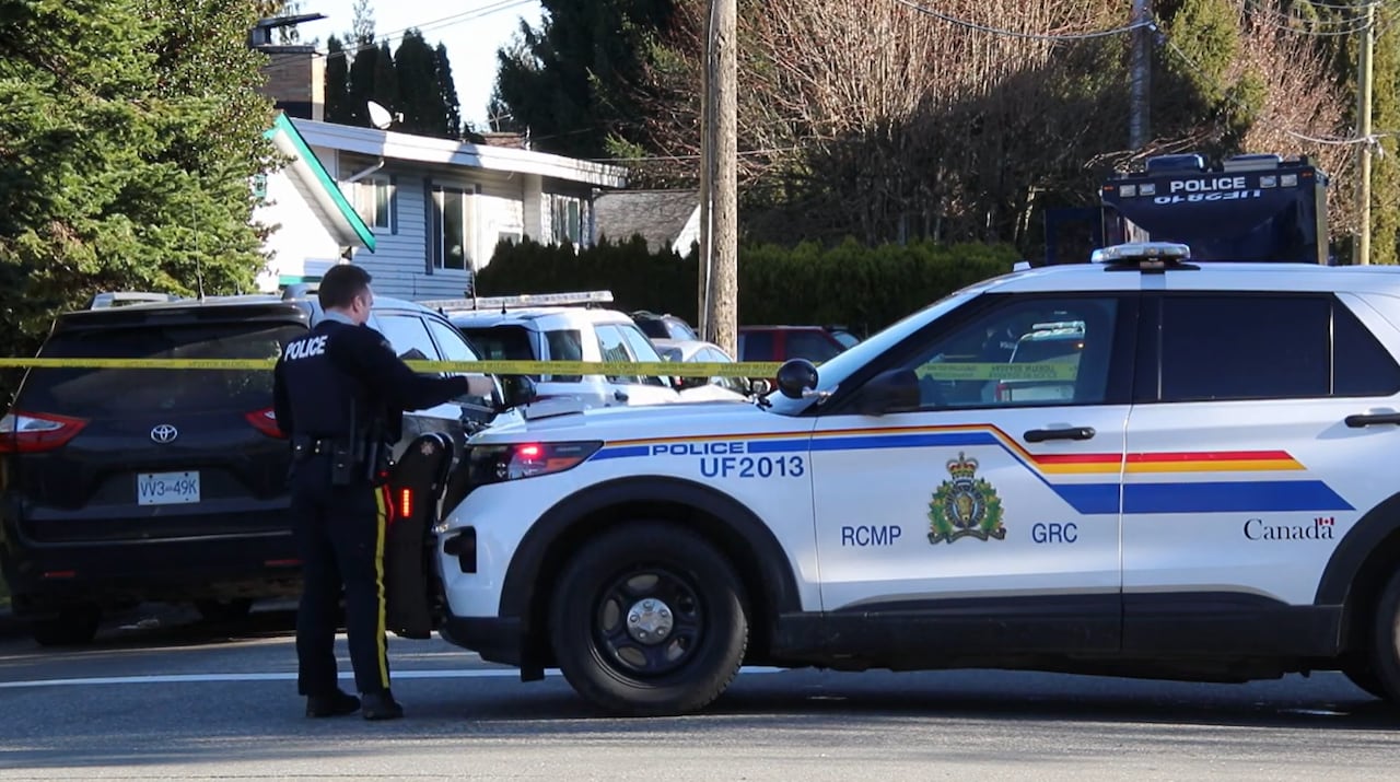 An RCMP officer stands beside a police vehicle on a residential street blocked off by police tape.
