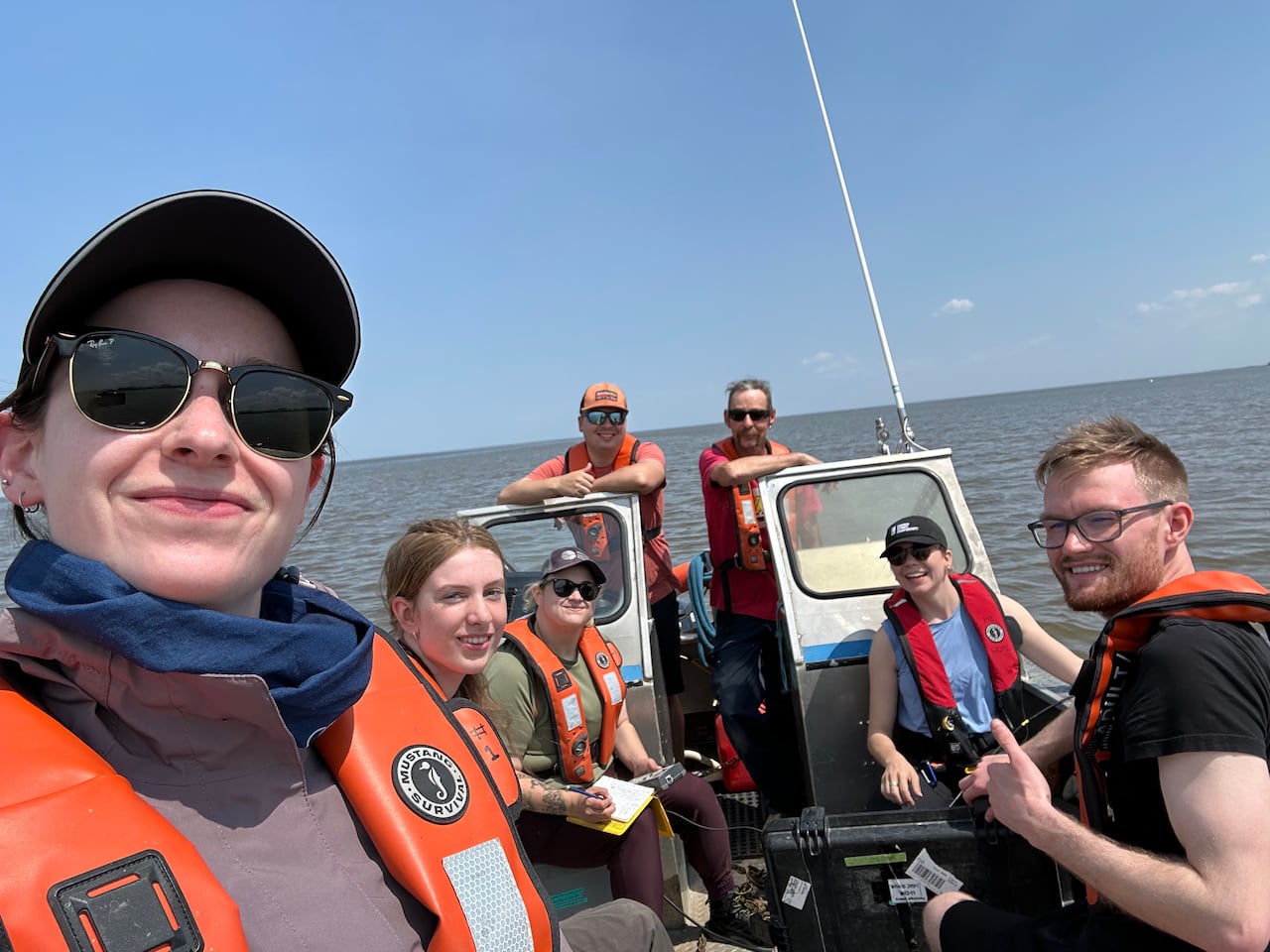Seven people pose for a selfie on a boat on a lake in the summer.