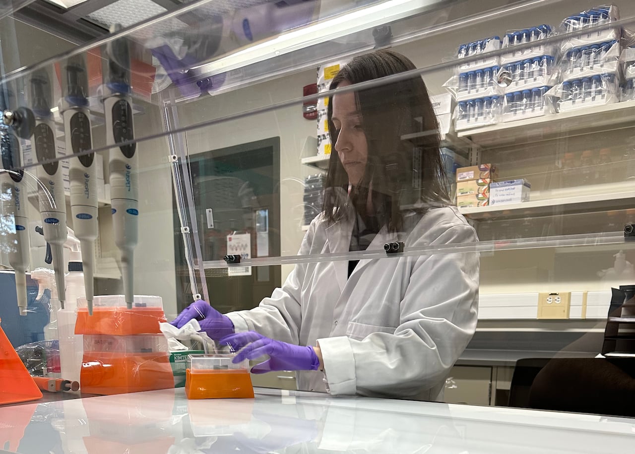 A scientist wearing a lab coat and purple gloves works in a lab.
