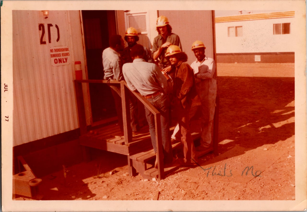 A photo of a group of oil workers standing at their worksite, wearing their uniforms. 