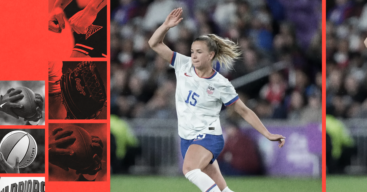 A female soccer player in a white USA jersey with number 15 is mid-stride on a grassy field, raising her right arm as she moves forward.