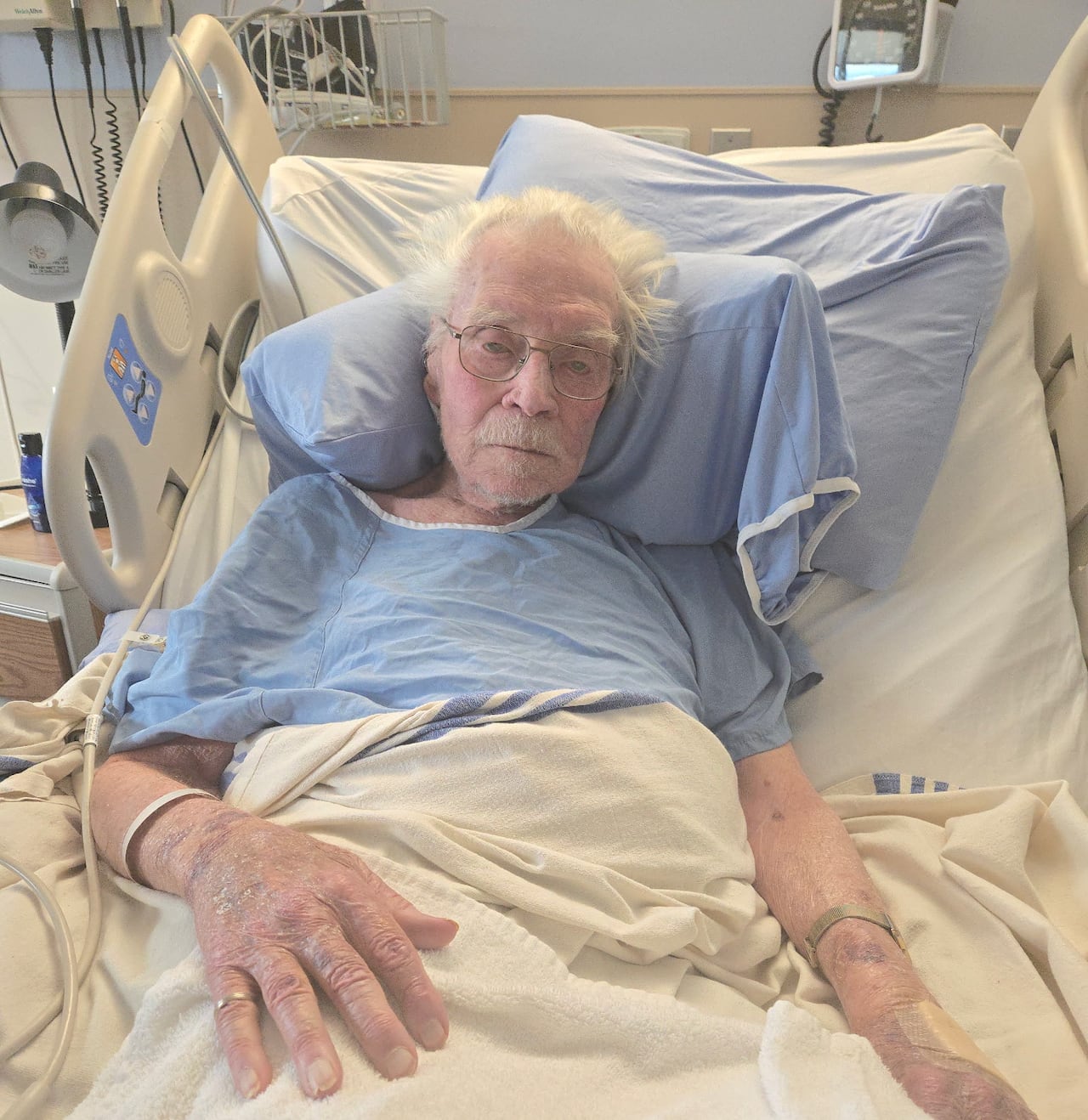 Man in blue gown lays in hospital bed.