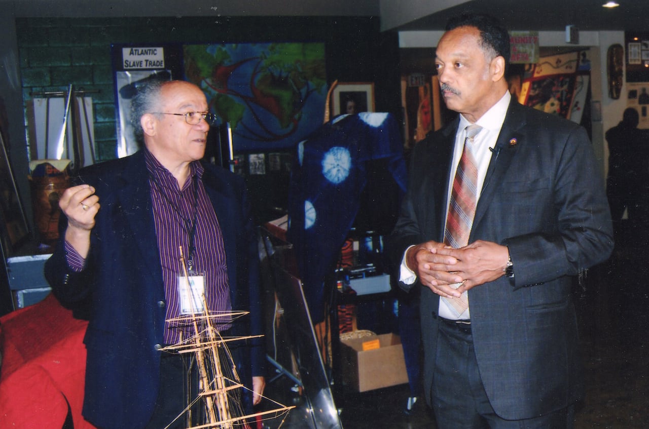 Two men stand next to each other near a model schooner