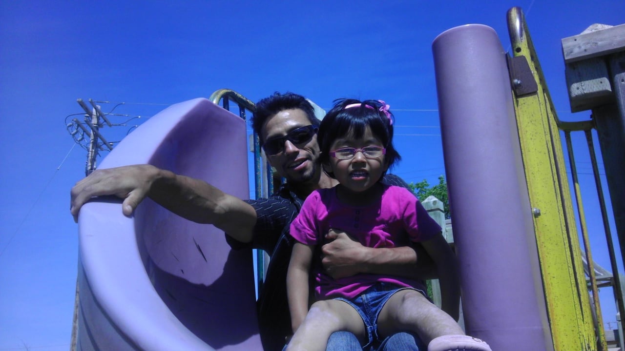 A man holds a girl on his arms as they go down a slide.