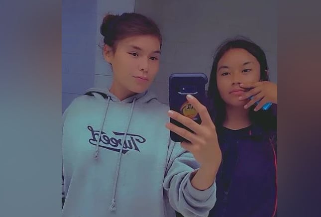 Two girls pose against a mirror, holding a phone.