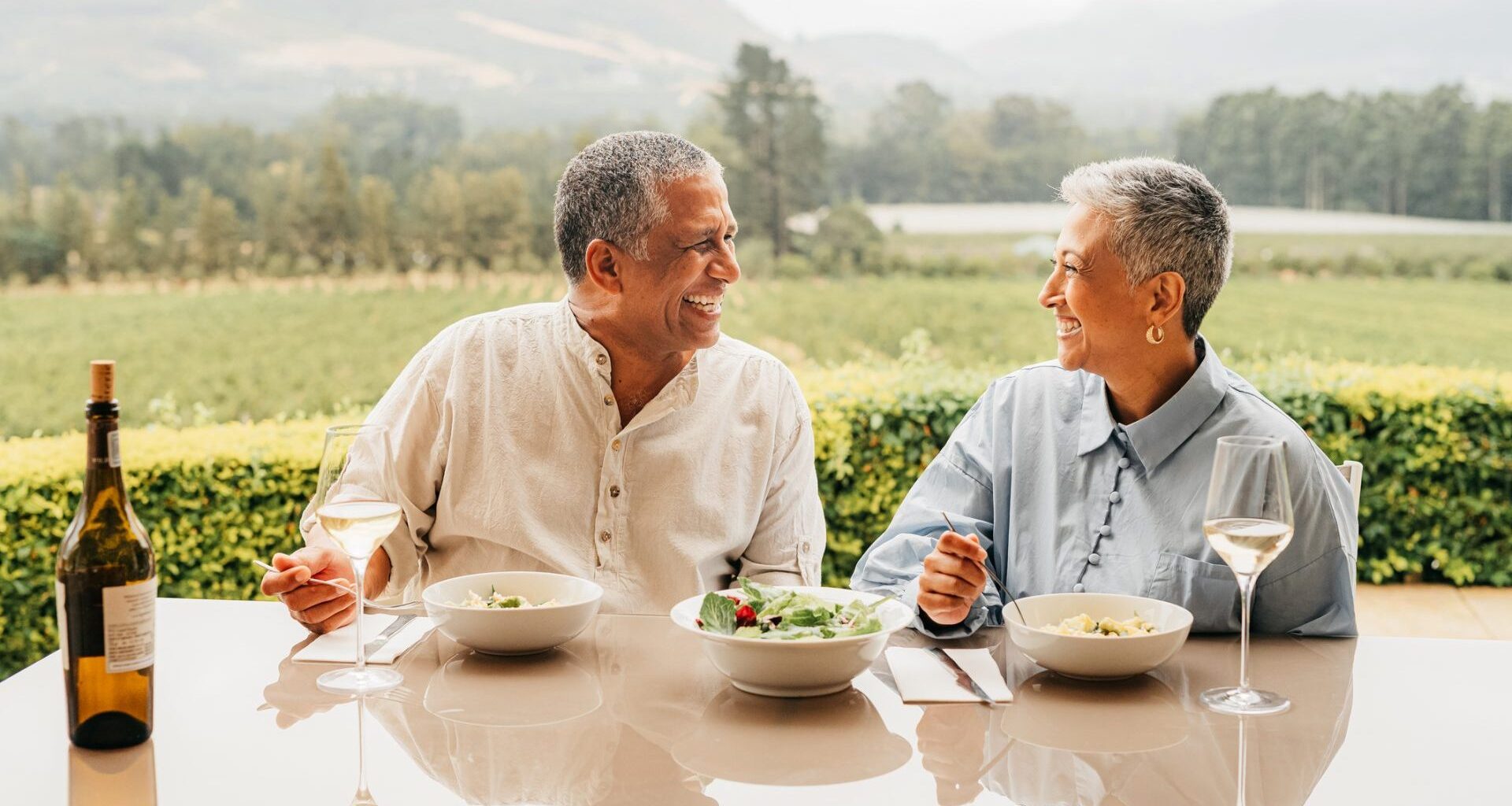 A rich couple sitting at a table together looking at each other while eating lunch at a vineyard
