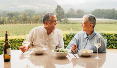 A rich couple sitting at a table together looking at each other while eating lunch at a vineyard