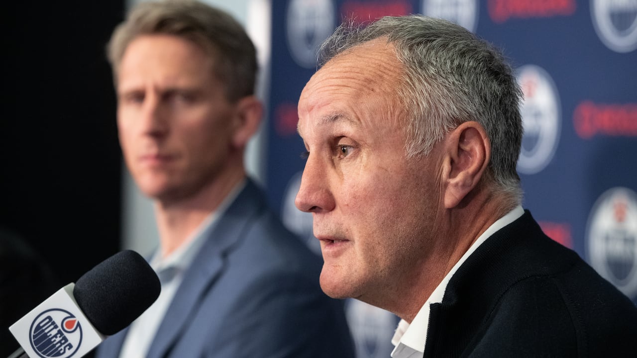 Two men sit in front of a microphone at a news conference.