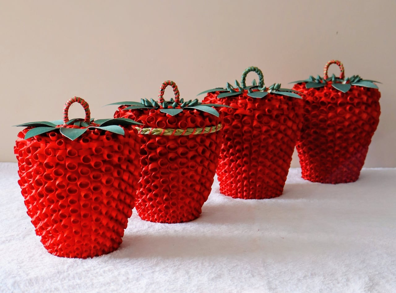 A line of four traditionally woven red baskets, shaped like strawberries, in front of a white background.