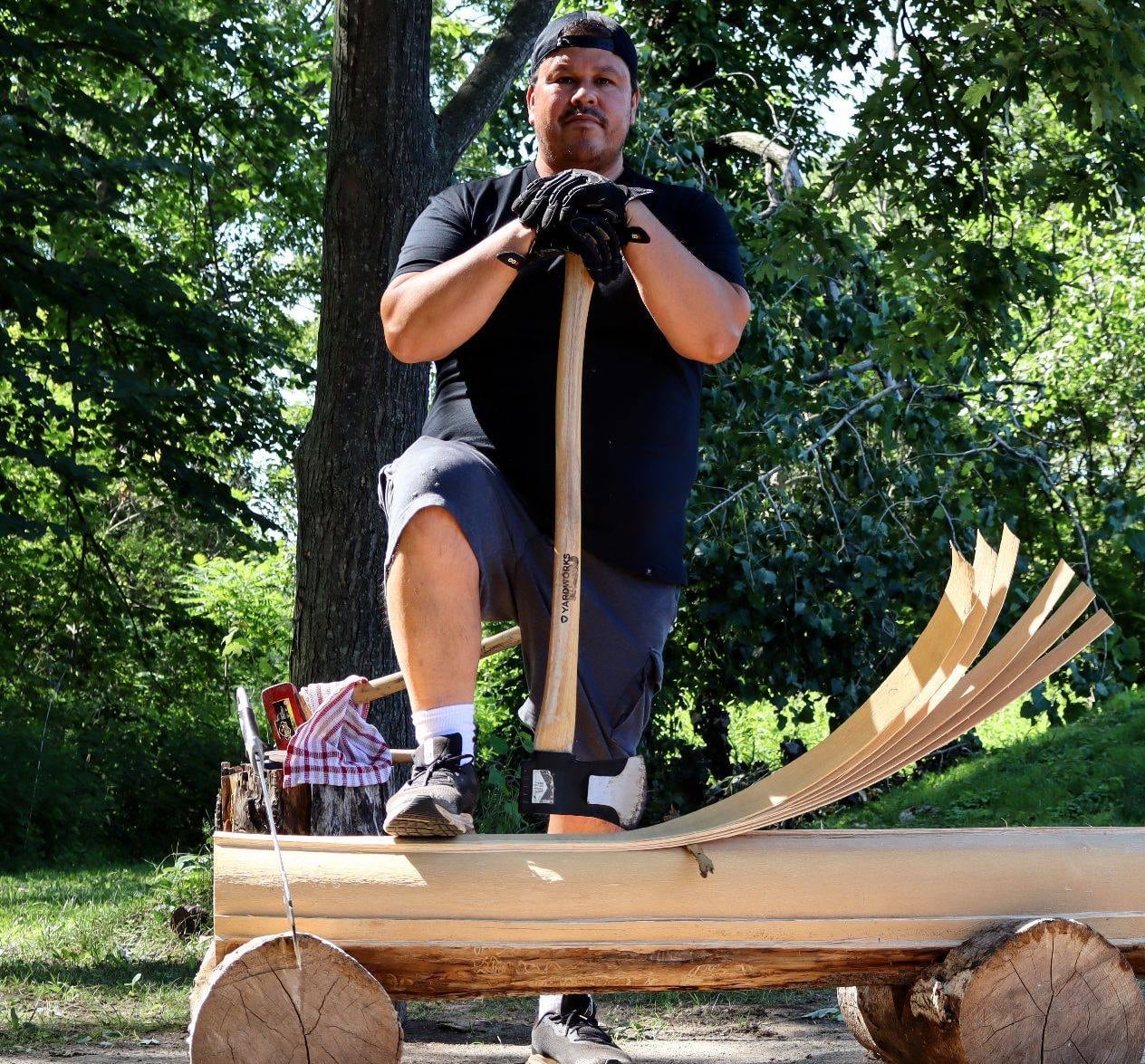 An Indigenous man holding an axe, with one foot on a log that is being carved into thin splints for basket making
