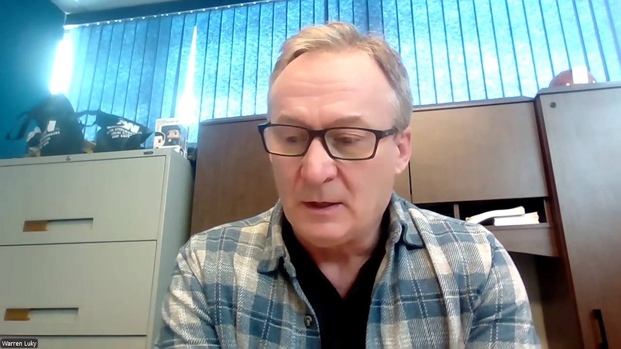 A man in a flannel shirt and glasses answers a question in an office.