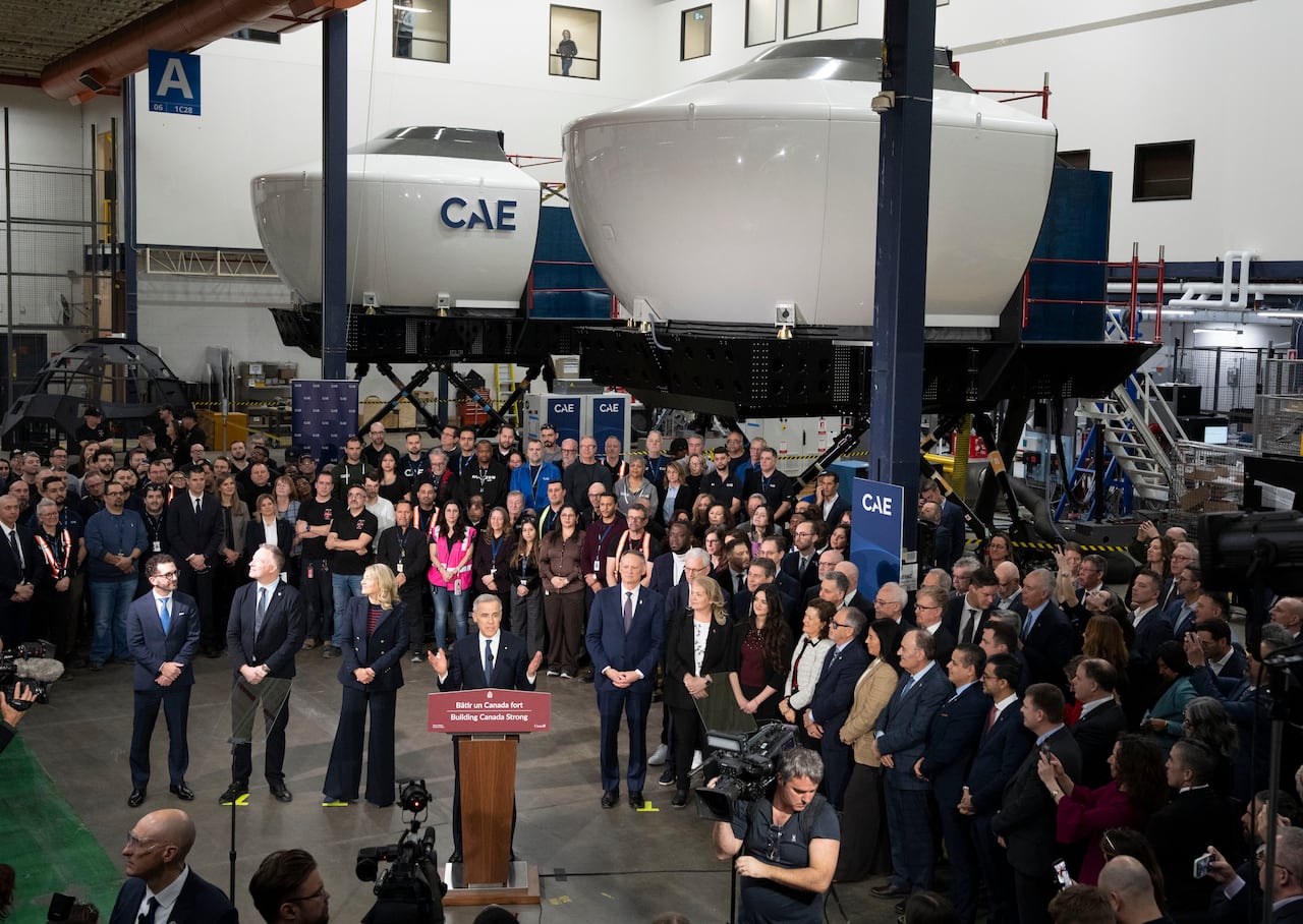 A man at a lectern stands in the middle of a crowd of people in a large hanger.