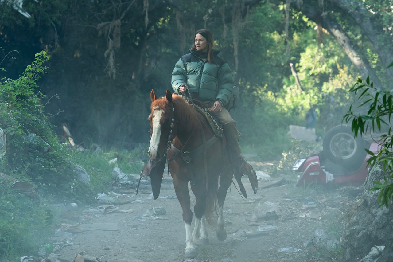 A woman on a horse rides through the forest.