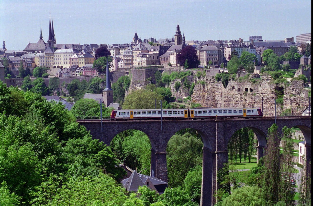An old European city with churches, steeples and a train crossing a bridge in the foreground.