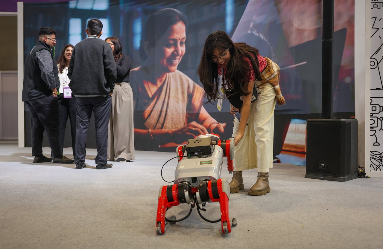 A woman in glasses leans down to greet a two-legged robot.