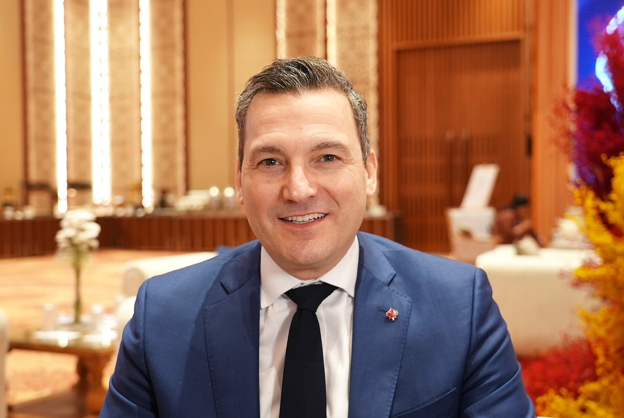 A man in a blue suit sits smiling.