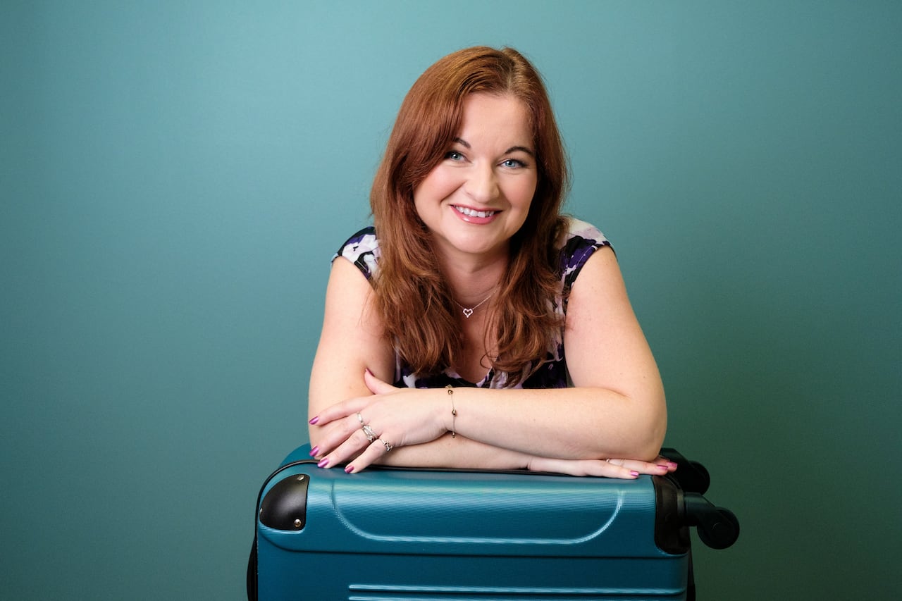 Woman with red hair smiling and leaning on blue suitcase