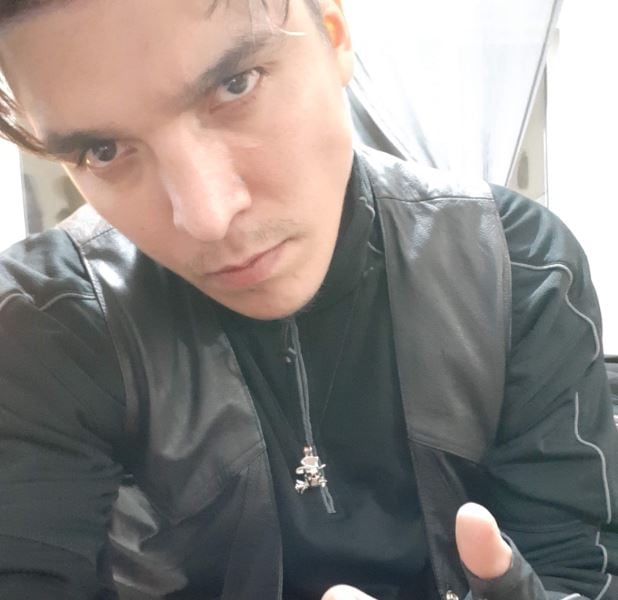 A man wearing a black jacket looks at the camera in a selfie.
