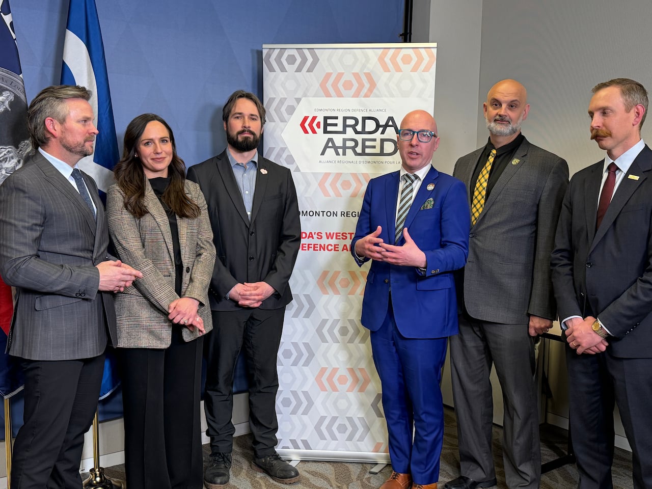 Five men and a woman stand before a banner that depicts the Edmonton Region Defence Alliance