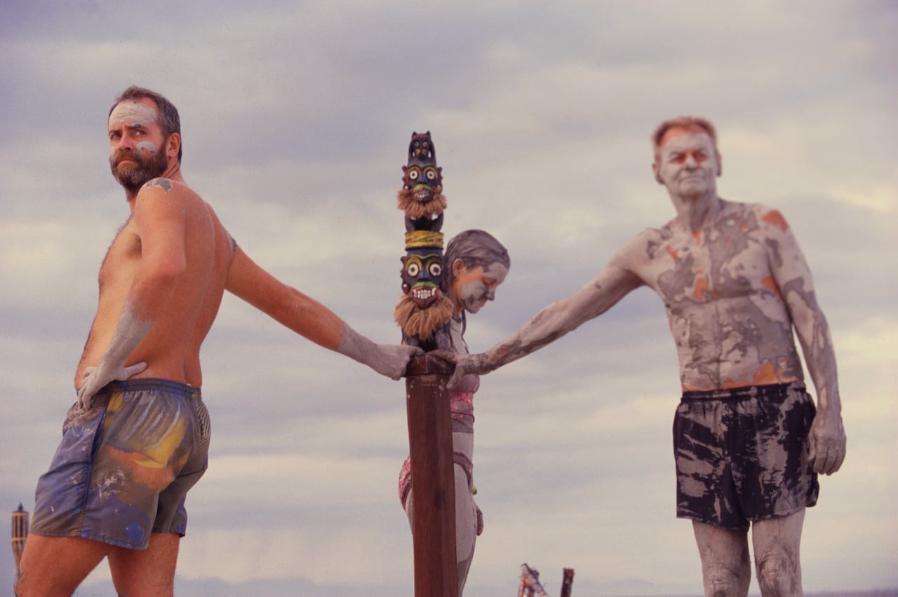 Three people stand holding a pole.
