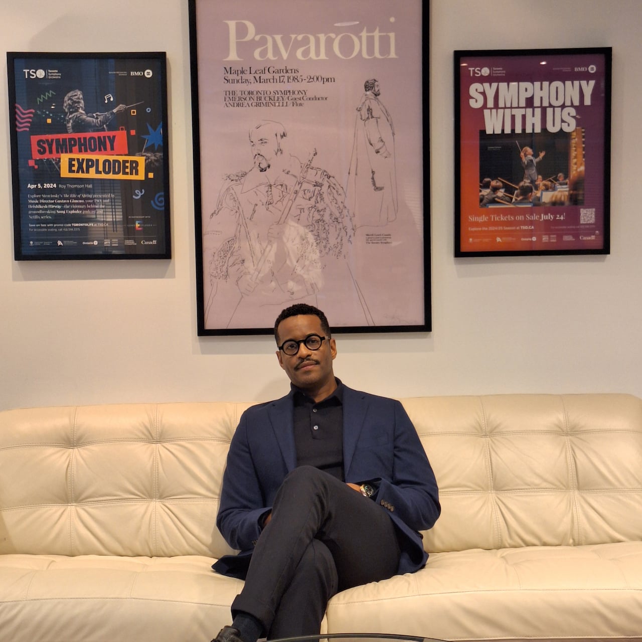 A man sits on a couch in front of three paintings.