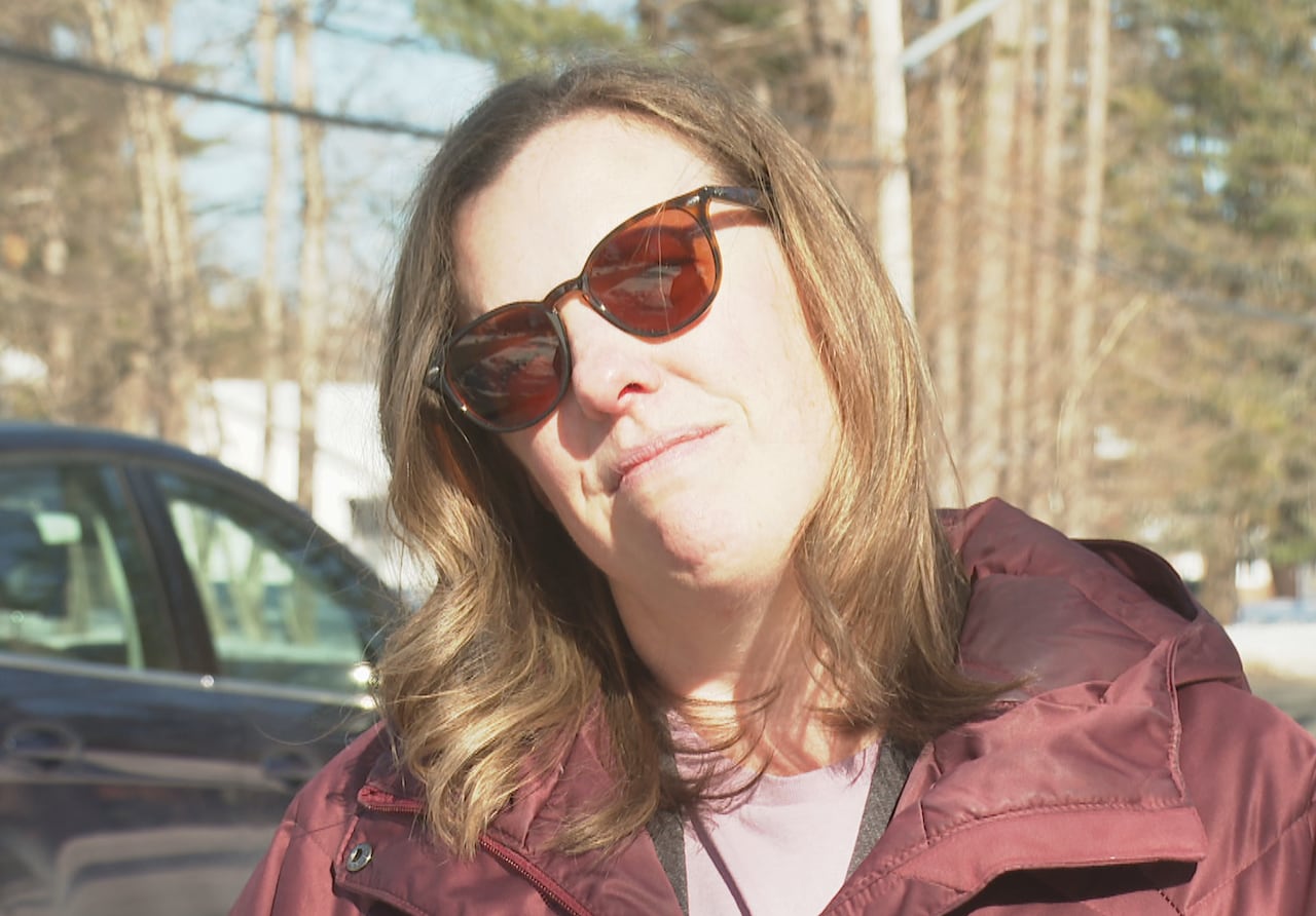 A woman with a neutral expression is wearing sunglasses and has brown hair.