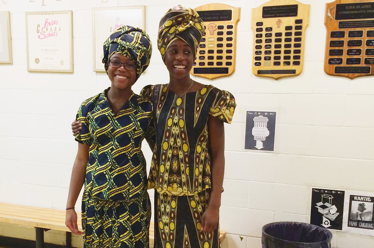 Two Black girls in yellow and black patterned dresses and head scarves.