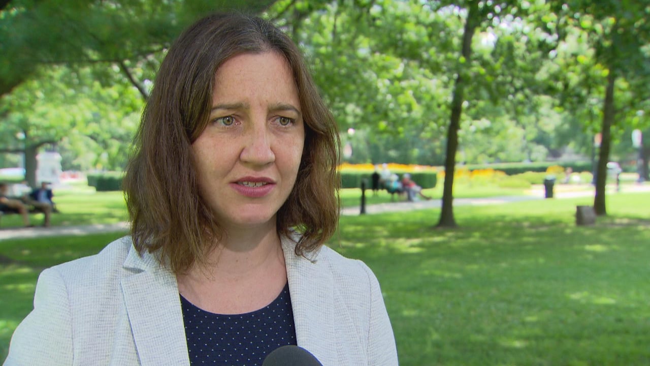 A woman wearing a white jacket looks out into a park.