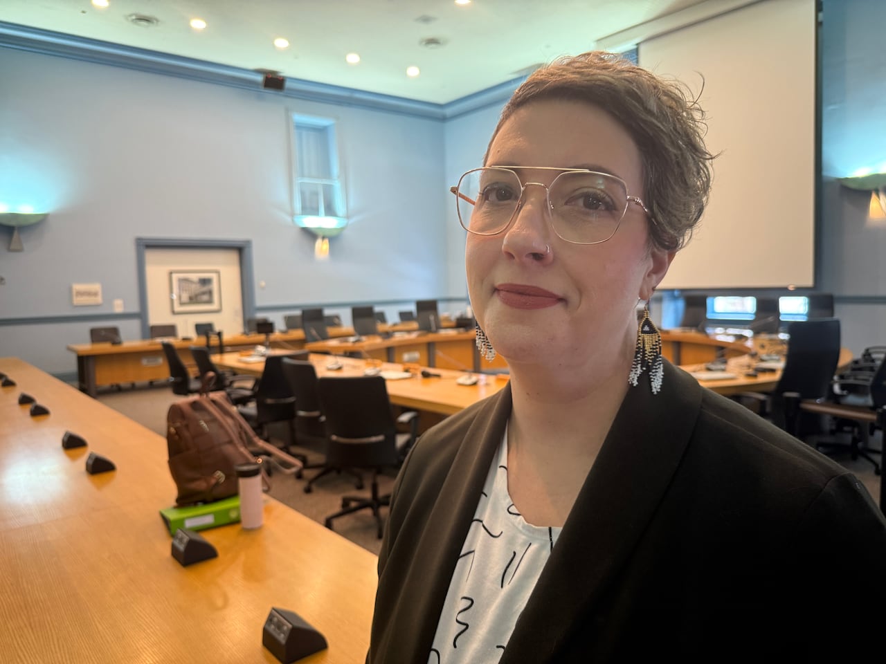 A photo of a woman wearing glasses inside a city committee meeting room