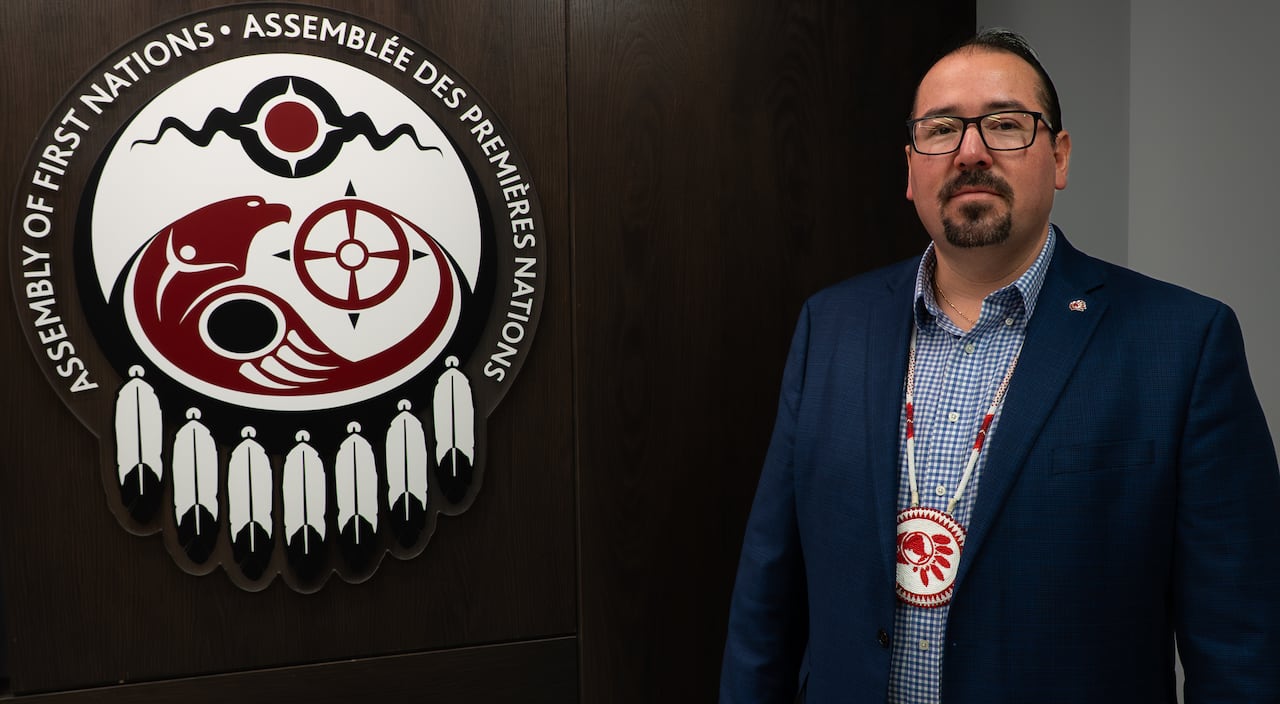 A chief stands in front of a logo.