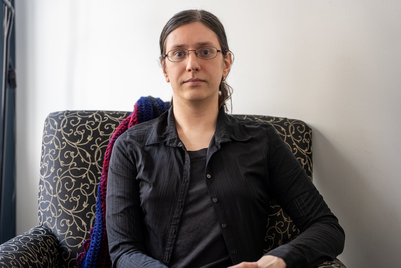 A woman on a black armchair with a neutral expression.