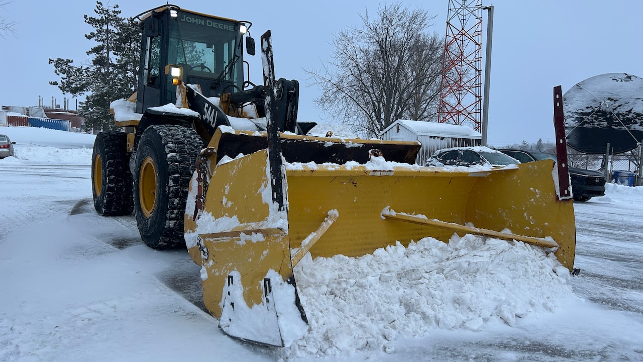 A snow plow sits in a snowy parking lot
