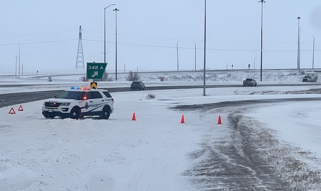 RCMP cruiser parked on a snowy highway with its lights on and orange pylons blocking the road.