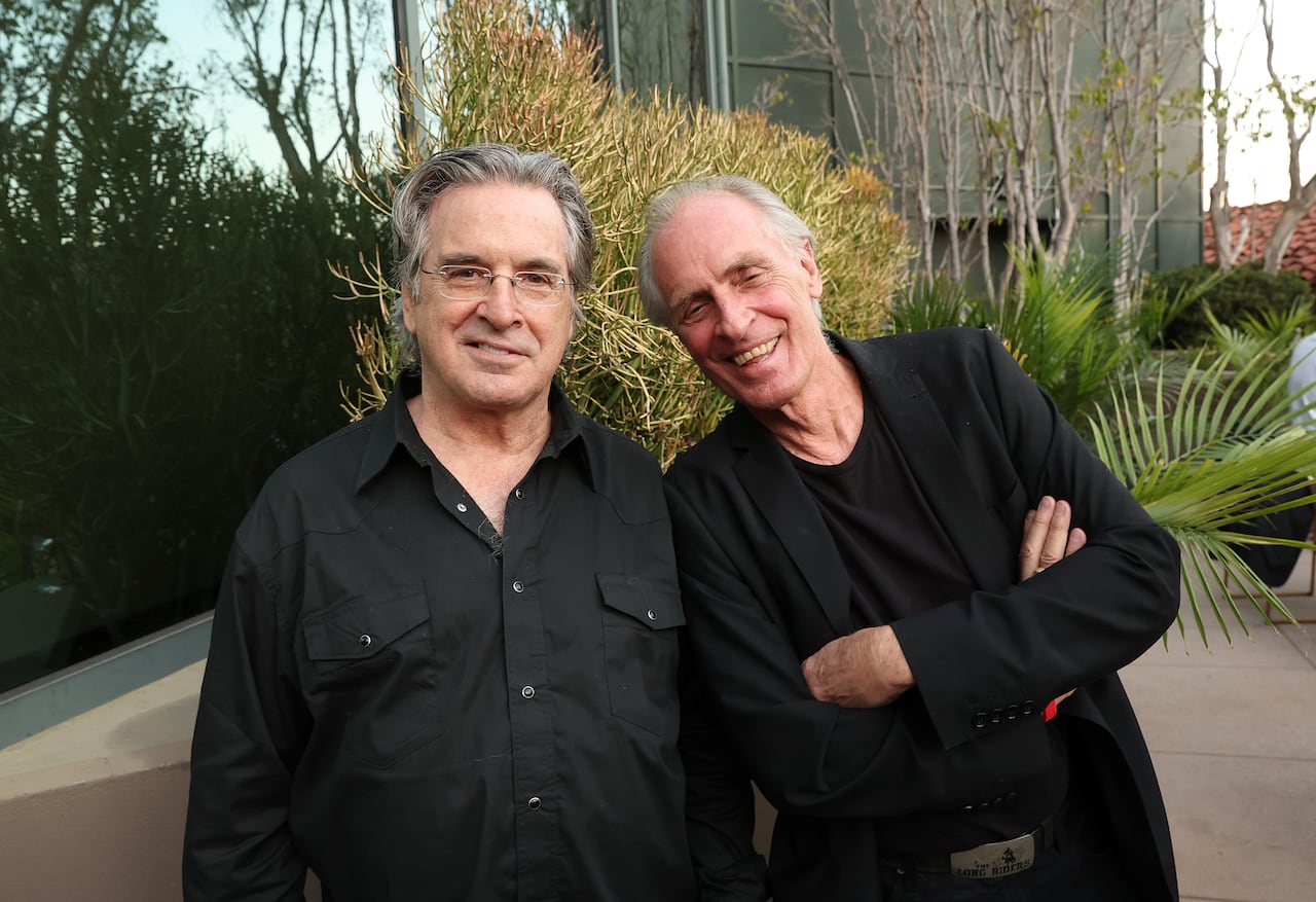 Two men in black pose for a photo in an outdoor setting