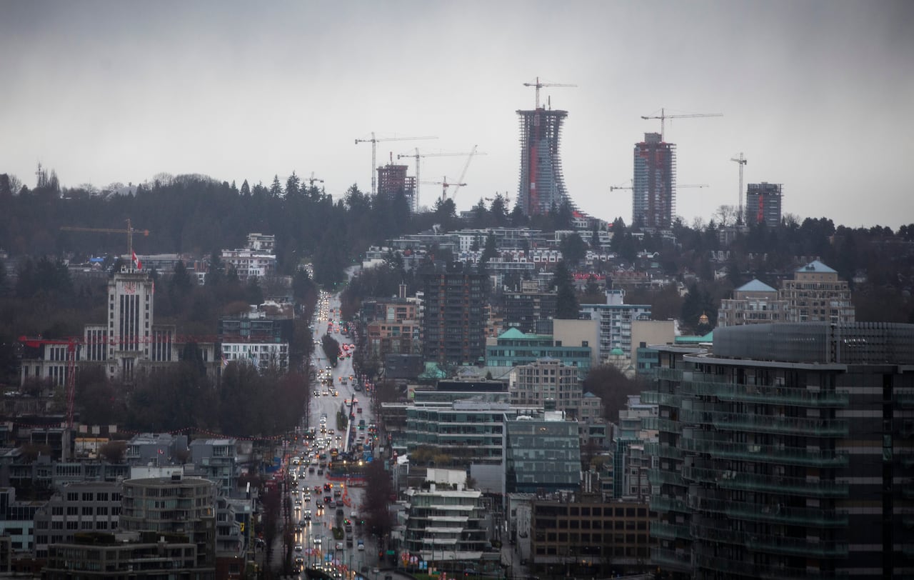 Under-construction skyscrapers are seen in the skyline on a rainy day, next to a busy road.